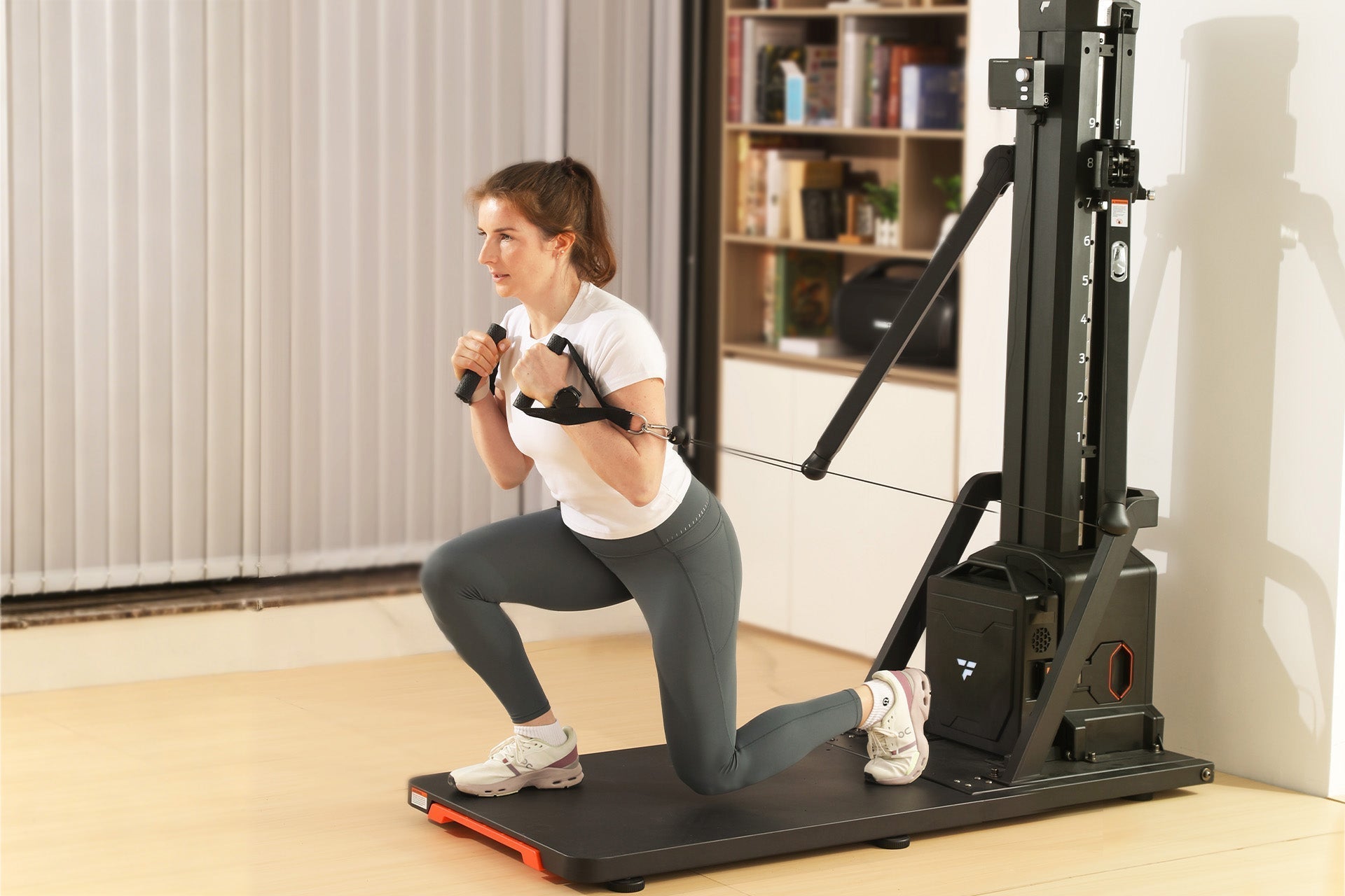 A woman in a white t-shirt and grey leggings performing a lunge on a smart home gym platform