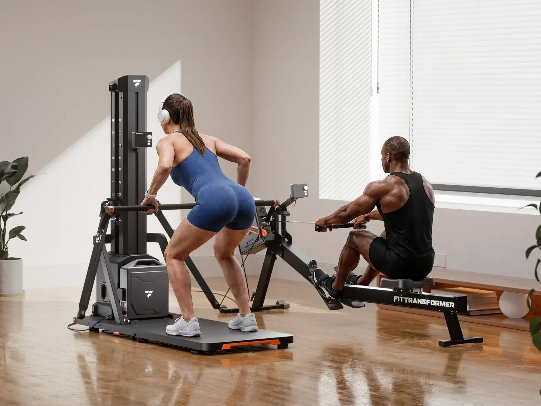 Couple working out together at home; woman in blue bodysuit with white headphones does bent-over pull exercise on vertical gym station, Black man in black tank top rows on detachable rowing module of FITTRANSFORMER all-in-one fitness machine beside her